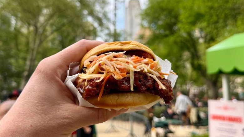 A close-up of a hand holding a BBQ Boneless Baby Back Rib Sandwich from Shake Shack