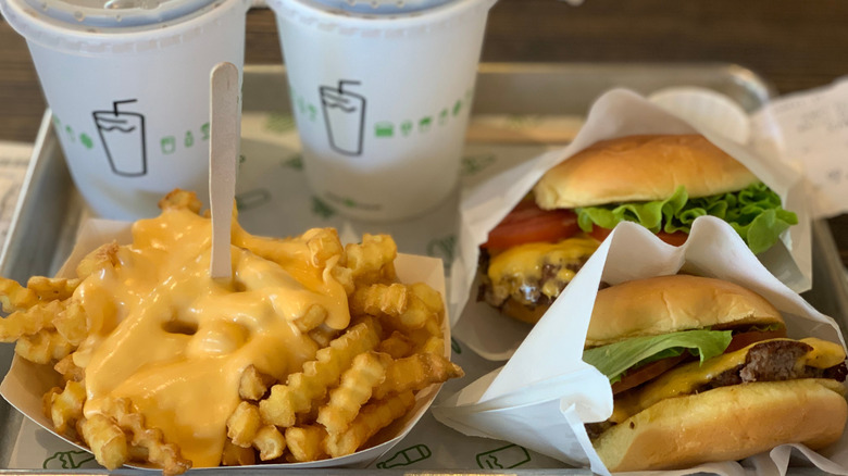 A plate of Shake Shack food with two burgers, cheese fries, and two drinks