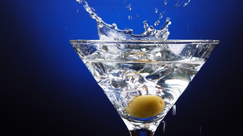 An olive splashing into a Martini with a blue background