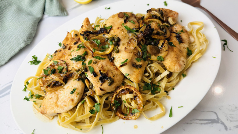 Lemony chicken piccata on serving platter over pasta