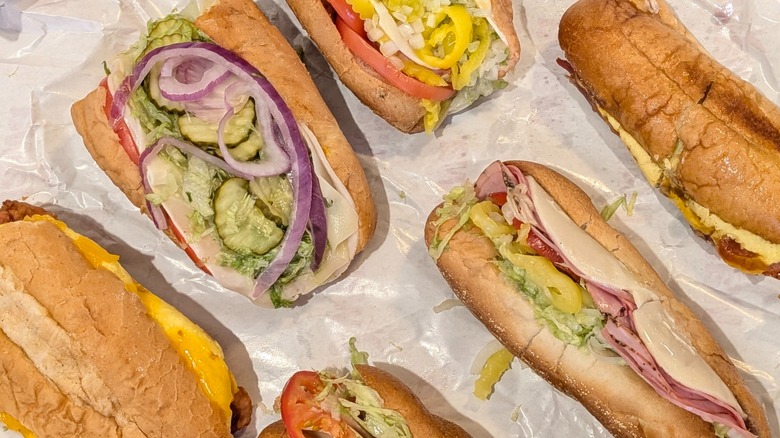 A close-up of six small subs lined up on wax paper