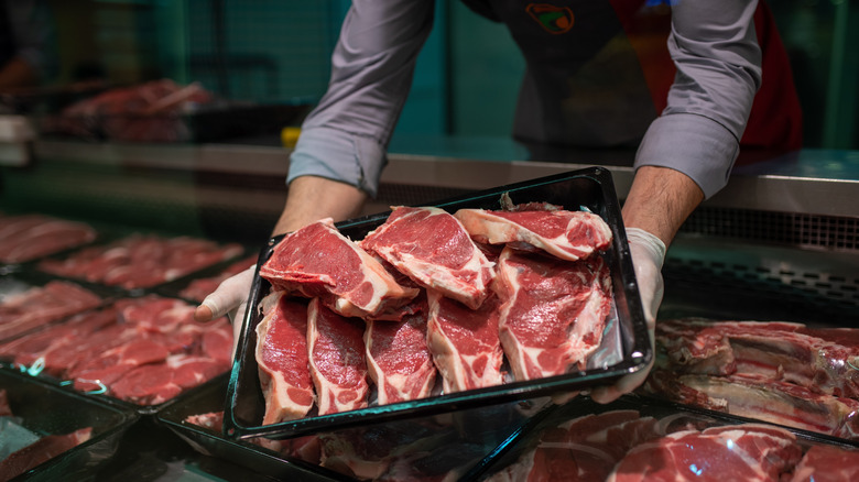 grocery butcher with big platter of cut steaks