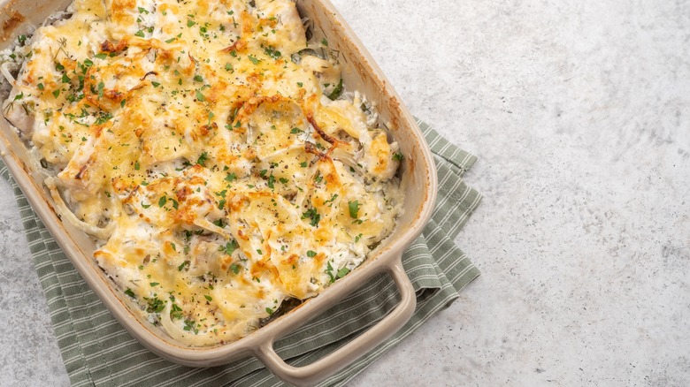 A baked casserole sitting in a dish, with baked cheese and herbs on top