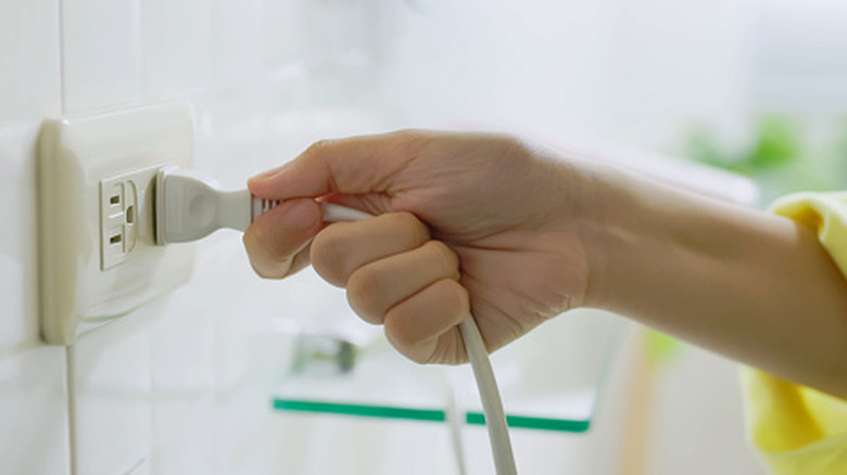 A person holding a plug in an outlet