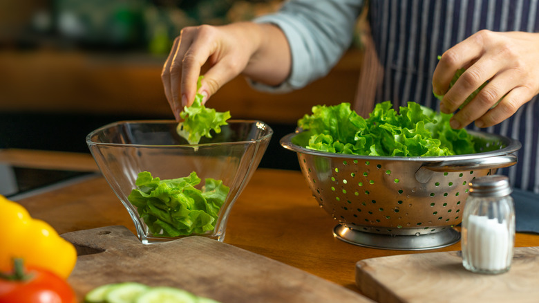 person placing lettuce in glass bowl