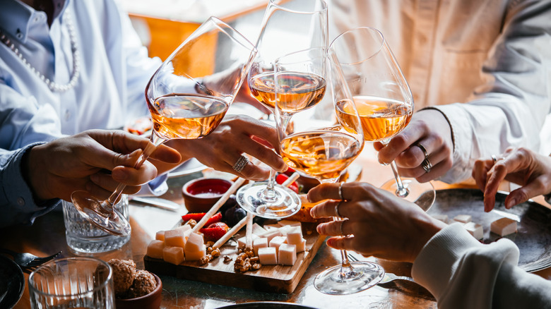 Guests clinking wine glasses at dinner party.