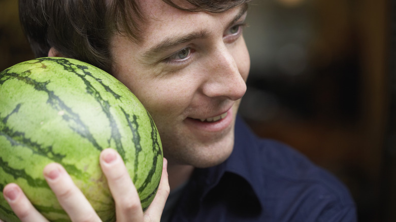 man tapping and listeneing to a watermelon