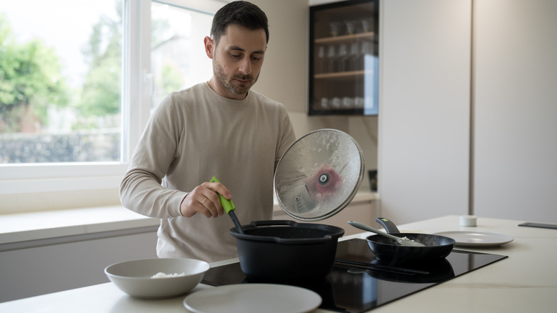 man in a white long-sleeved shirt, cooking on an induction stove with an abstracted expression