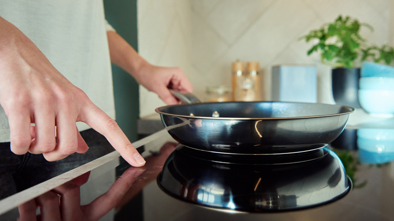woman's hand choosing a power level on her induction stove with one hand, and holding a skillet on its gleaming, smooth surface with the other
