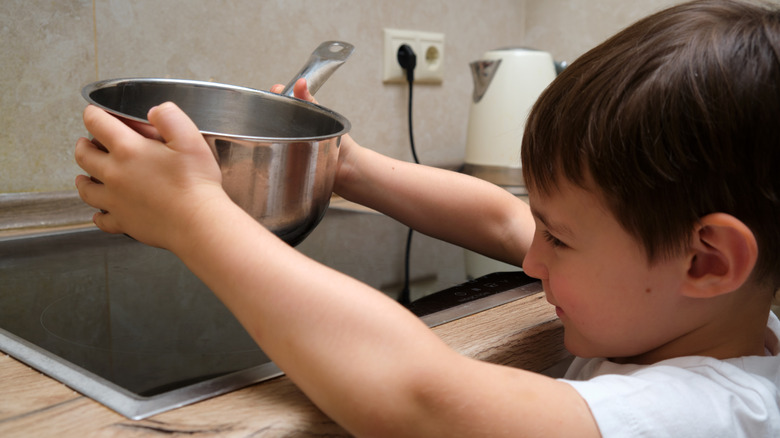 young boy putting a pot onto an induction cooktop