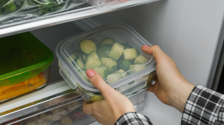 person putting a chopped zucchini in a glass container in fridge