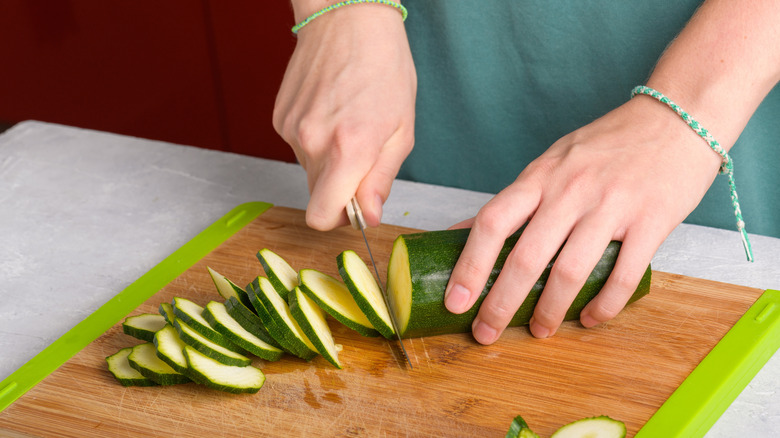 hands slicing zucchini on a wood board