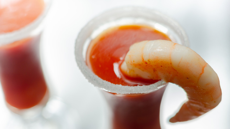 A poached shrimp hanging out of a salt-rimmed shot glass full of red liquid
