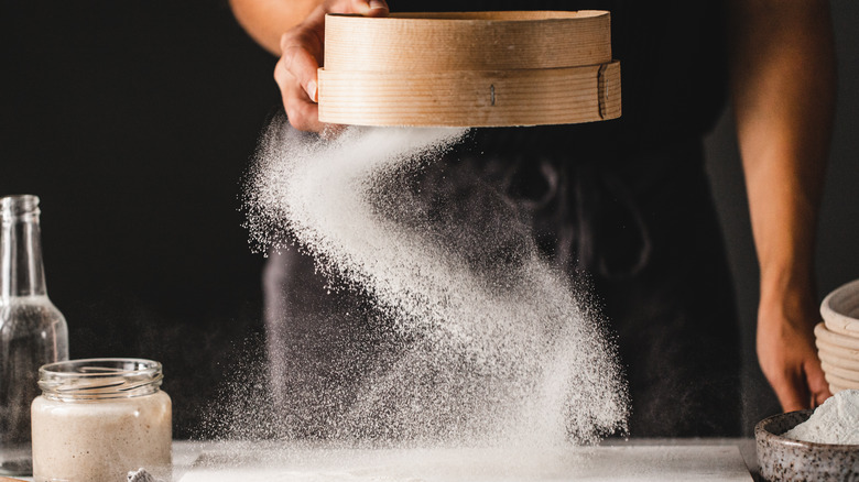 Someone using a tamis sifter for flour over a marble board