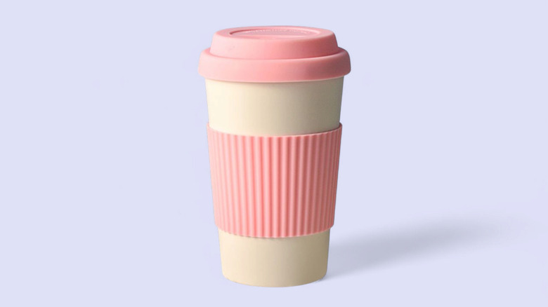 Reusable coffee cup with pink silicone lid on purple background