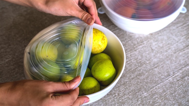Person placing silicone lid over bowl of fruit