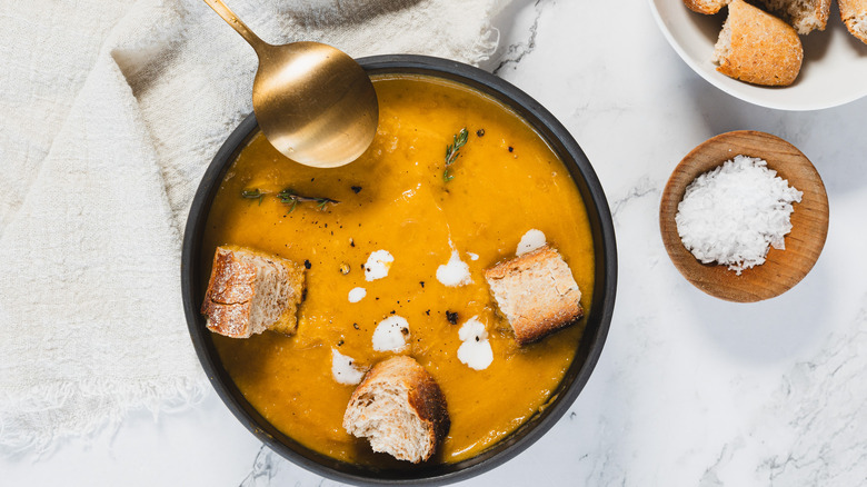 Overhead bowl of carrot soup with spoon, croutons and salt