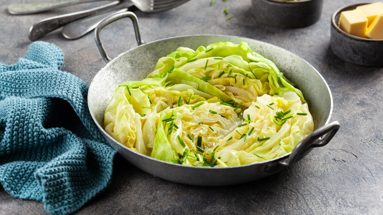 A silver bowl of cooked cabbage next to a blue kitchen towel