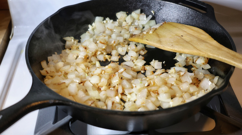 cast iron skilet full of sauteed onions and garlic with wooden spatula