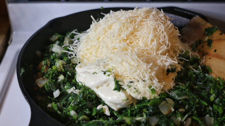 ricotta and grated parmesan cheese atop skillet of cooked greens and onions