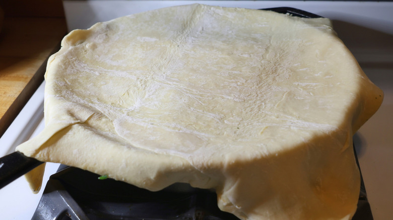 cast iron skillet on stove with sheet of puff pastry draped overtop