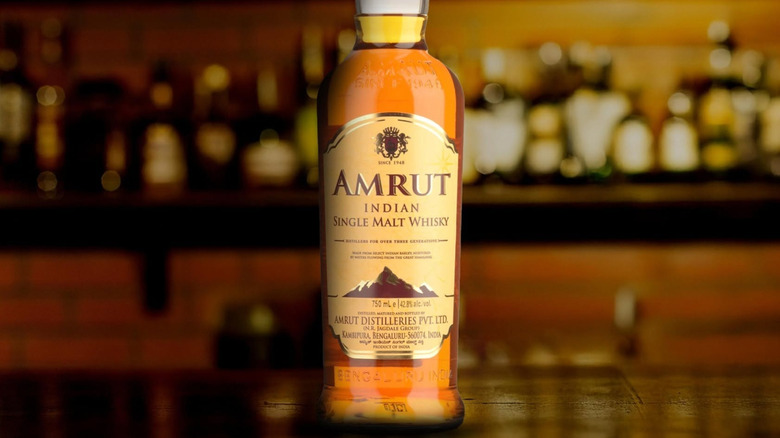 A bottle of Amrut Single Malt Whisky posed on a bar with blurred bottles in the background