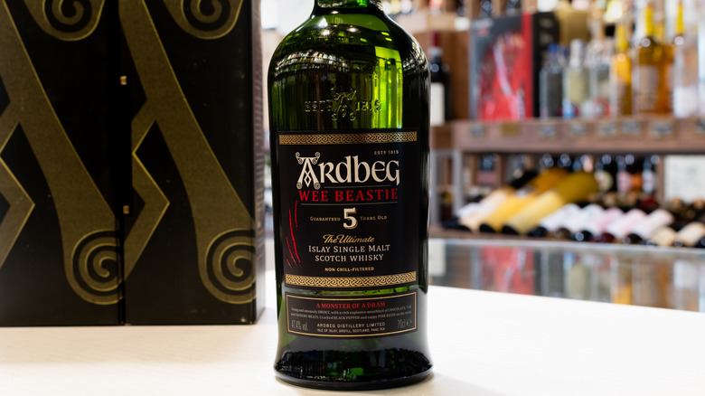A bottle of Ardbeg Wee Beastie posed in a liquor store with blurred bottles shown in the background
