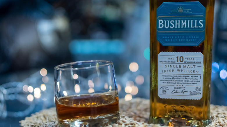 A bottle of Bushmills 10-year placed on a pile of grain next to a filled glass