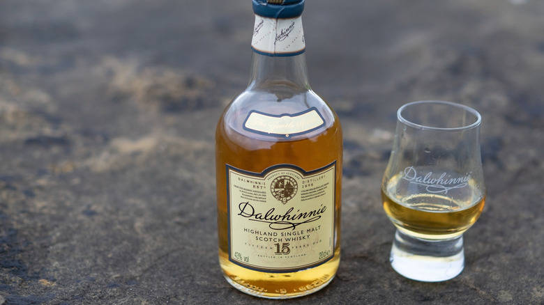 A bottle of Dalwhinnie 15-year on a rocky surface posed next to a filled branded glass