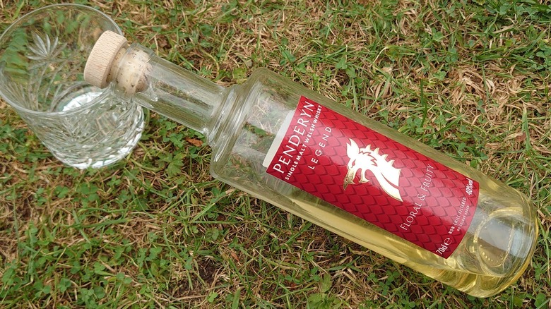 A bottle of Penderyn Legend balanced on the rim of a glass with a grassy background