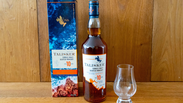 A bottle of Talisker 10-year on a wooden surface with an empty glass and its box sitting on either side
