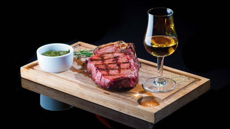 Steak and stemmed glass of whiskey on cutting board