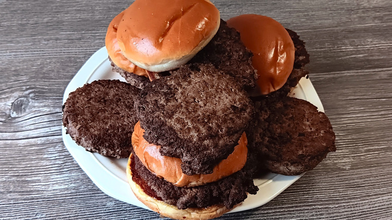 Plate piled high with burger patties, some with buns, on a wooden tabletop