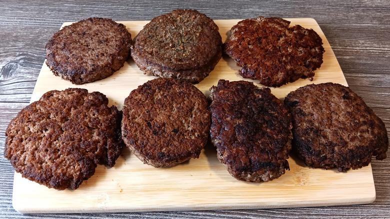 Two rows of seven burger patties from sit-down chain restaurants on a cutting board