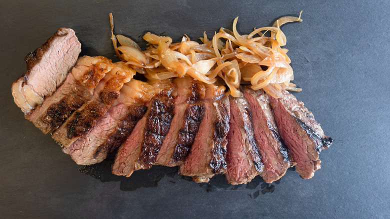 thin sirloin steak on surface with sauteed onions