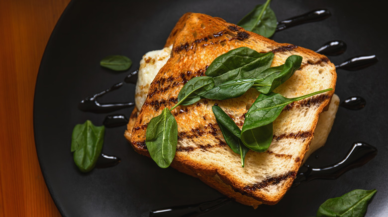 A toasted sandwich drizzled with balsamic glaze and mozzarella poking out
