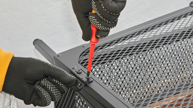 Closeup of personal installing a grill with a screwdriver.