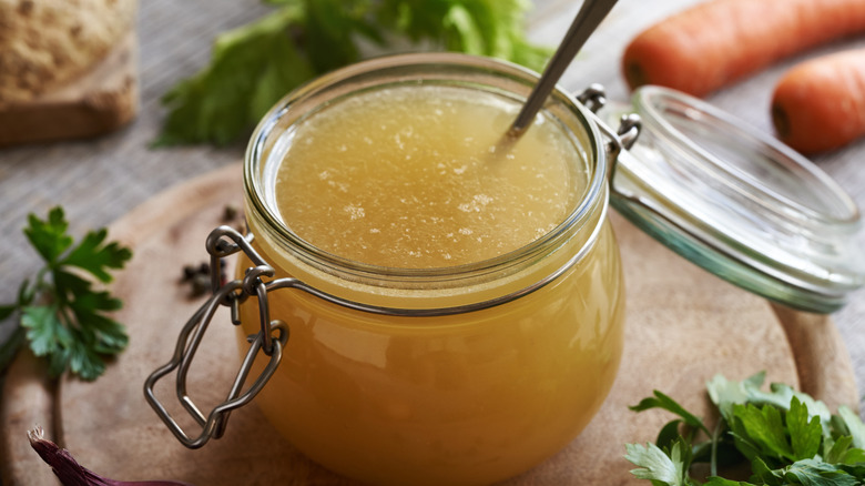 A jar filled with homemade stock surrounded by mirepoix ingredients