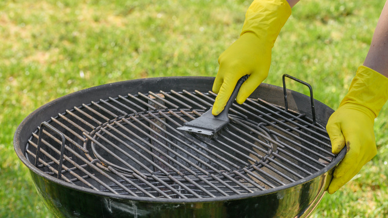 Person wearing rubber gloves cleans outdoor grill with brush