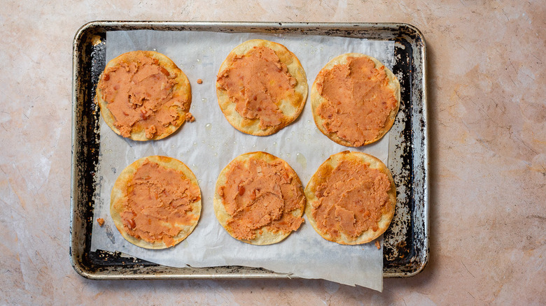 Baked tortillas with refried beans on baking sheet