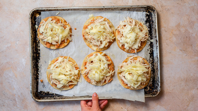 Tortillas with refried beans, cheese and chicken on baking sheet