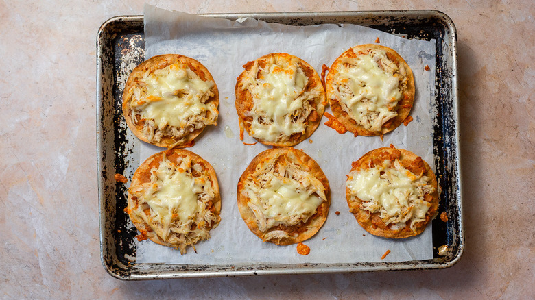 Baked tortillas with refried beans, cheese and chicken on baking sheet