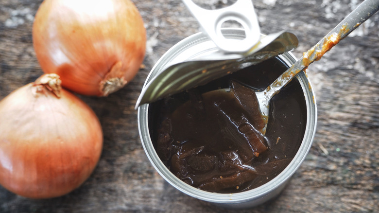 An open can of soup with two onions next to it
