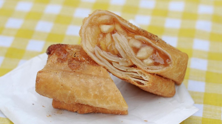A fried apple pie made with apple filling and a tortilla cut in half on a yellow checkered tablecloth