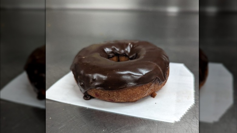 A chocolate cake donut with a thick layer of icing on top of a wax bag