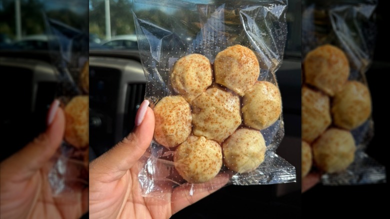 A woman's hand holding a Cinnamon Cream Cheese Pull Apart donut wrapped in plastic