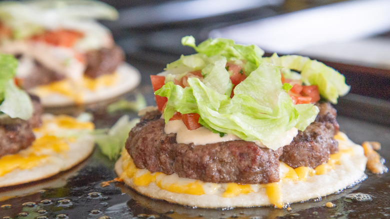 Burger on tortilla and cheese topped with lettuce and tomatoes