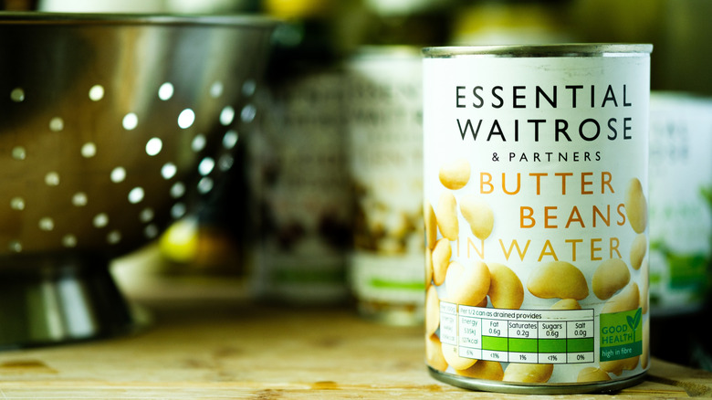 Can of Waitrose butter beans in water on a kitchen counter next to a colander
