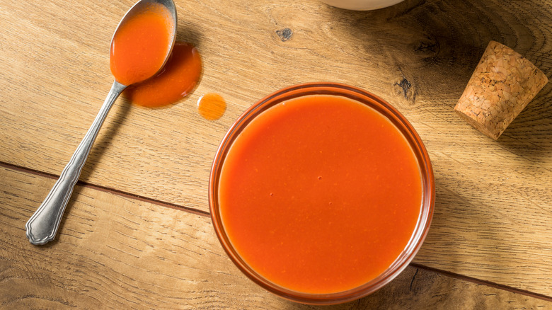 Buffalo sauce in small cup with a spoon full of the sauce lying next to it.