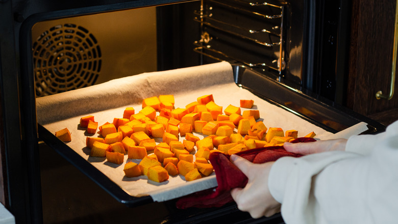 person removing a tray of cubed pumpkin from a convection oven